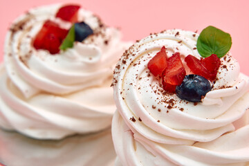 Delicious meringue dessert with fresh berries and chocolate on pink background