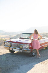 beautiful girl in a retro dress at sunrise happy posing on the background of the mountain landscape in Cappadocia near a red retro car