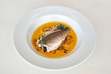 Exquisite grilled sea bass with mussels in saffron sauce on white plate