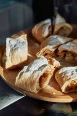 Delicious homemade apple strudel with powdered sugar on wooden plate in sunlit kitchen
