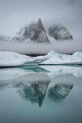 Serene Reflection of Snow Covered Mountains and Icebergs in a Misty Fjord