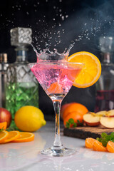 Cocktail glass with fruit drink forming a splash of fresh oranges and lemons with mint and bottles with colored liquids 