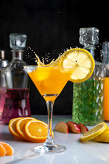 Cocktail glass with fruit drink forming a splash of fresh oranges and lemons with mint and bottles...