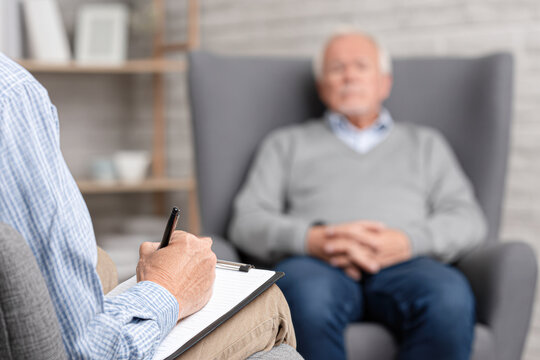 A therapist takes notes while an elderly man, seated in a chair, discusses his thoughts during a counseling session.