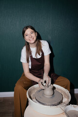 Smiling Caucasian woman making pottery in hobby ceramic studio with clay and apron