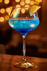 Refreshing blue cocktail with lemon garnish in elegant glass against warm light backdrop