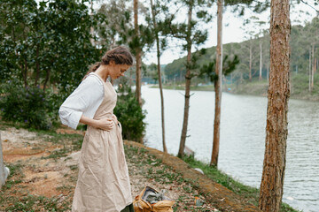 Young woman in a rustic dress standing by a serene river, showcasing nature s tranquility and a...