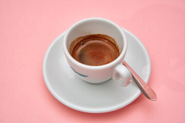 Fresh espresso coffee in white cup on pink background with silver spoon