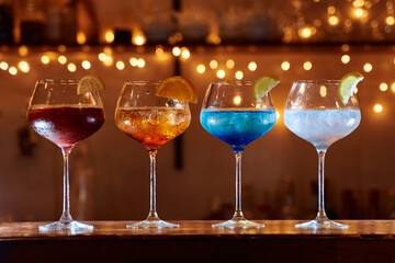Colorful cocktails in glasses with citrus garnish on a bar counter in dimly lit setting