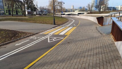 A tile sidewalk and two-lane bike with markings runs along the riverfront along the parapet, lawns,...
