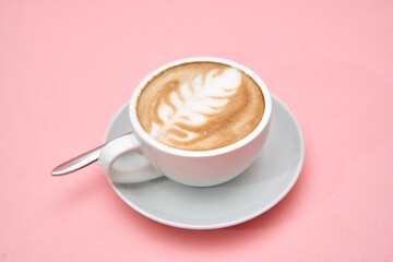 Elegant latte with leaf art in white cup on soft pink surface
