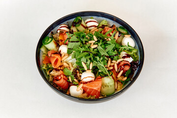 Fresh gourmet salad with arugula, salmon, mozzarella, and balsamic drizzle in black bowl