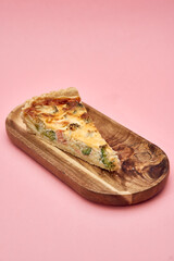 Delicious slice of homemade broccoli and cheese quiche on wooden plate against pink background