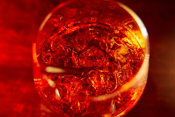 Amber cocktail with ice in glass on red background in low light setting