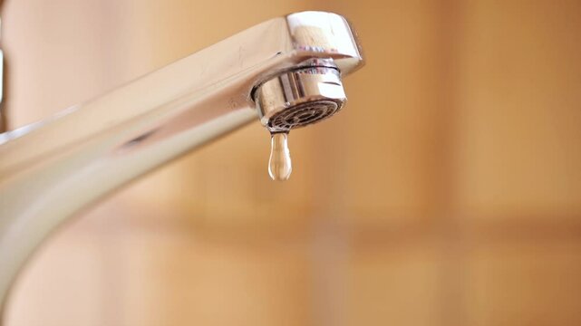 Slow motion dripping tap with water droplets inside apartment bathroom. Macro, close up, looking up shot, shallow depth of field, no people