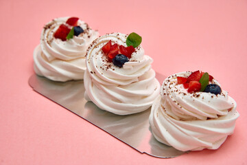 Delicious meringue trio with berries on pink background