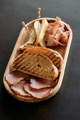Charcuterie platter with grilled bread, prosciutto, sliced pears, and smoked meats on wooden tray