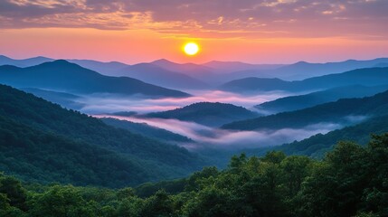 Obraz premium A vibrant sunrise illuminates layered mist-covered mountains with lush green forests under a colorful sky.
