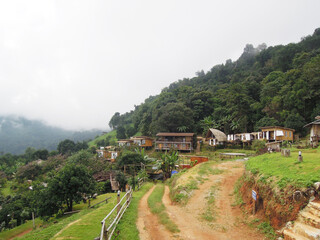 A rustic nature resort village nestled amidst lush green misty mountains and dense forests, with a...