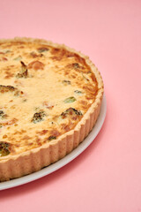 Savory broccoli cheese quiche on plate over pastel pink background