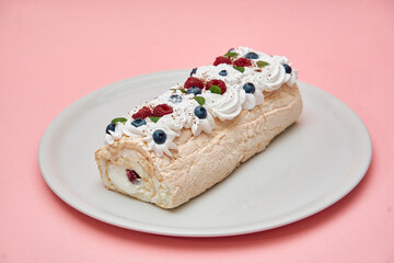 Elegant meringue roulade with fresh berries on a white plate with pink background