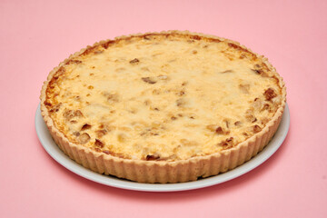 Classic quiche lorraine on white plate against pastel pink background