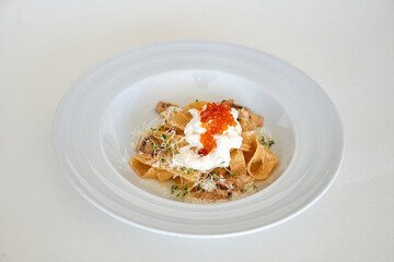 Gourmet pasta dish with cream, mushrooms, and roe garnish on elegant white plate