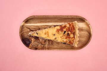 Wooden platter with slice of cheesecake on pastel pink background