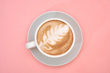 Latte art coffee cup on pink surface with leaf design capturing the essence of café aesthetics