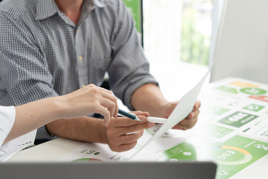 A diverse business team analyzing environmental charts and graphs in a collaborative meeting to create sustainable strategies in a modern office.