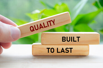 Quality Built to last text on green wooden blocks held by hand represents durability and long-term...