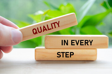 Quality in every step text on wooden blocks held carefully symbolizes continuous improvement and focus