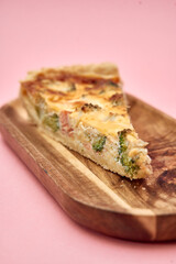 Delicious slice of broccoli and bacon quiche on wooden plate with pink background