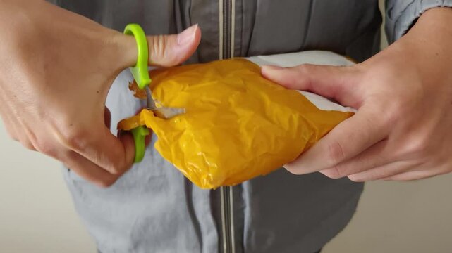 Close-up of a person's hands using scissors to open a yellow bubble mailer. Unboxing an online shopping order, e-commerce concept, package delivery service, and receiving a parcel from a store. 4k.