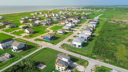 Colorful raised houses and RVs, trailers near Beach Boyt in Port Bolivar, Texas, large grassy lots and ocean views evoke relaxed coastal lifestyle blending vacation homes and storm-safe design