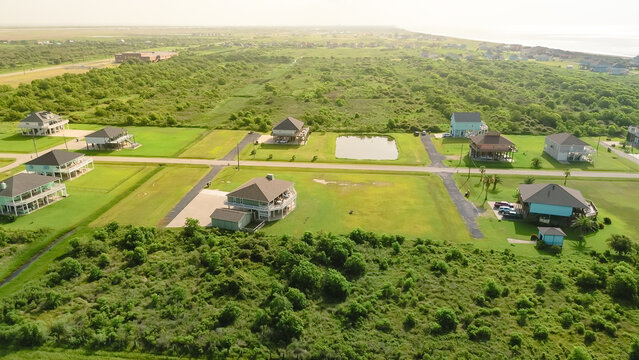 Scattered low tree bushes throughout terrain near shoreline Beach Boyt in Port Bolivar, Texas, balancing sandy setting with natural texture. Mix of established beach homes and undeveloped lots