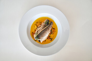 Elegant sea bass dish with aromatic sauce and herbs on white plate