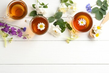 Aromatic herbal tea in glass cups, different flowers and green leaves on white wooden table, flat lay. Space for text