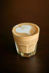 Rich coffee with heart-shaped latte art in glass cup on dark wooden background