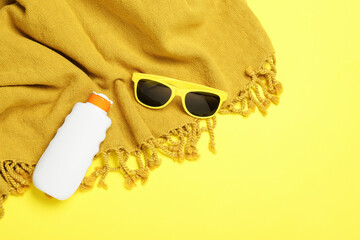 Beach towel, sunglasses and sunscreen on yellow background, flat lay. Space for text