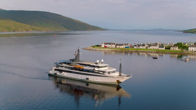 Cruise ship Variety Voyager arrives in Ullapool, sailing past small coastal houses with a stunning view north toward Ben Mor Coigach mountain under clear skies.