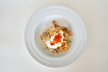 Gourmet pasta dish with mushrooms, caviar, and herbs on white plate