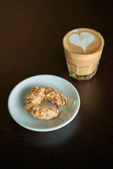 Cappuccino with heart latte art and almond cookie on dark wooden table
