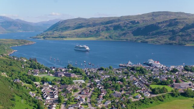 Drone shot of Viking Sun cruise ship anchored in the loch near Ullapool, with stunning views of the village, surrounding mountains, and clear blue skies on a beautiful day.