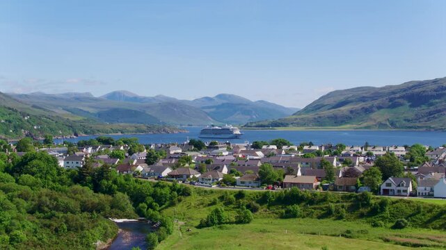 Low-to-high drone shot revealing Viking Sun cruise ship anchored in Loch Broom with Ullapool village unfolding in the background, framed by mountains and coastal scenery.