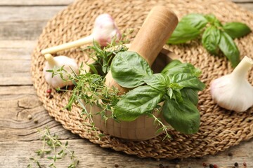 Mortar with pestle, different aromatic herbs and spices on wooden table, closeup