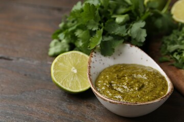 Tasty sauce with cilantro and lime on wooden table, closeup. Space for text