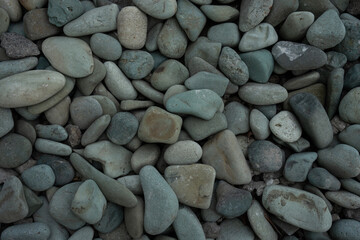 A close-up shot of various smooth, grey and teal pebbles, creating a natural texture background.