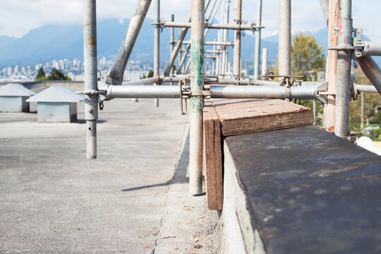 Scaffolding blocking or cribbing on wall or rooftop. Temporary wood support structure on parapet wall to distribute weight and stabilize scaffold structure. Flat roof with city view. Selective focus.