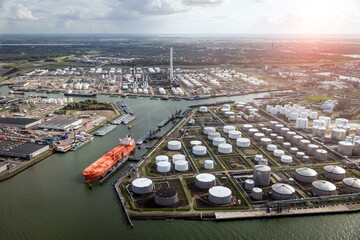 Aerial view of a large orange oil tanker moored at an oil storage silo terminal in an industrial port.